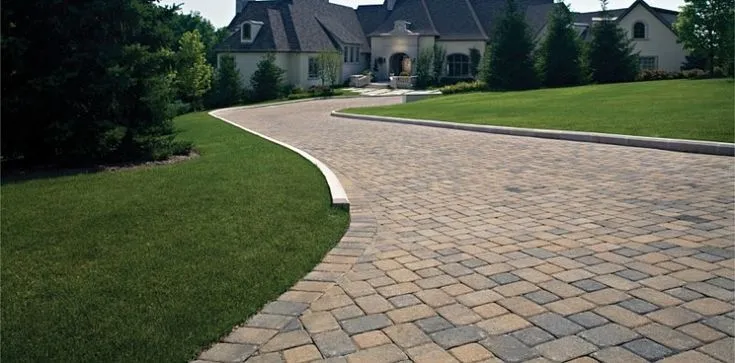 A paved driveway leading to a house with a green lawn.